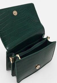 Grön läderhandväska med en strukturerad yta, som har en guldknapp för stängning och dragkedjor inuti för organisering.