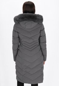 Grå pufferjakke med faux fur-krave, chevron-quiltet mønster og mellemlang design. Har en hætte og lange ærmer.