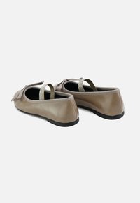 Zapatillas de ballet beige con cuero sintético liso, suelas negras y detalle decorativo de lazo. Incluye tiras para el tobillo en verde claro con adornos.