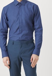 Tmavě modrá košile s dlouhým rukávem, límcem na knoflíky, strukturovanou látkou a odpovídajícími kalhotami, které mají úzký střih a poutka na pásek.