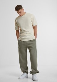 Lys beige bomull t-skjorte med korte ermer, kombinert med avslappede olivengrønne sweatpants og hvite sneakers med elastiske mansjetter.