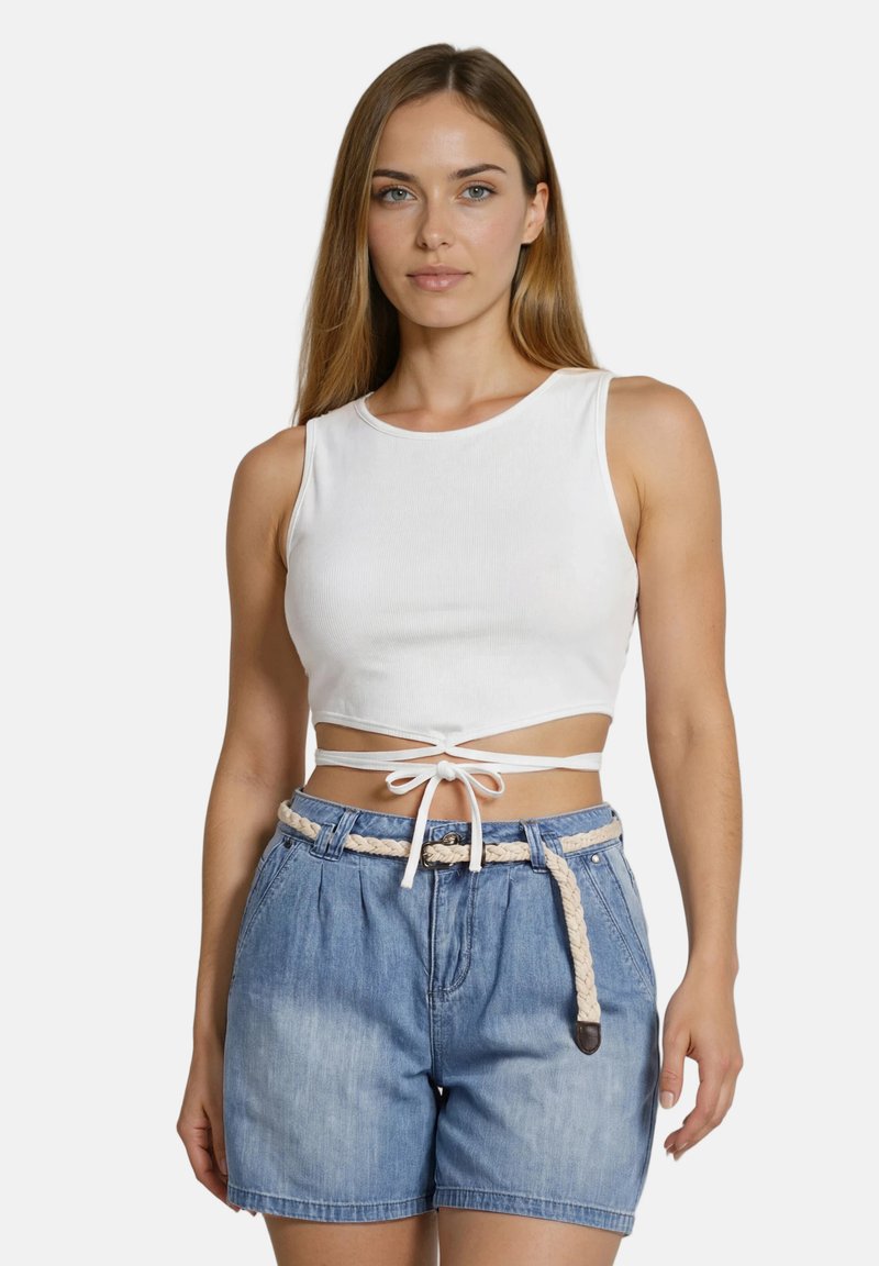 Γυναίκα που φοράει λευκό αμάνικο crop top με δέσιμο μπροστά και τζιν σορτς με ψηλή μέση και πλεγμένη ζώνη σχοινιού, στέκεται μπροστά σε απλό φόντο.