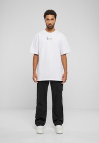 Hvit bomulls t-skjorte med korte ermer og et svart grafisk trykk på brystet, kombinert med svarte cargo bukser og hvite sneakers.