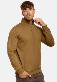 Brun sweatshirt med halv-zip krave, ribbede manchetter og kant. Har et diskret logo på brystet. Blød tekstur, afslappet pasform.