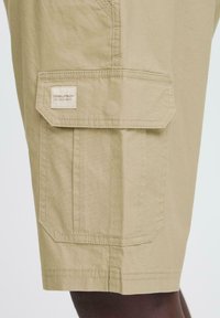 Lys beige cargo shorts lavet af holdbart stof, med en klaplomme med et broderet logo, synlige sømme og en afslappet pasform.