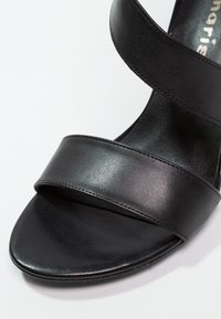 Sandale en cuir noir avec deux larges brides, une texture lisse, un design à bout ouvert et une forme épurée et minimaliste.