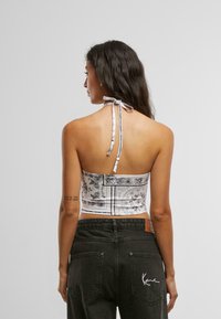 Fehér pántos crop top fekete virágmintákkal, megkötős nyakkivágással és testhez simuló fazonnal. Magas derekú sötét farmerral párosítva.