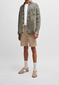 Chemise en denim gris clair portée sur un t-shirt blanc, associée à un short beige et des baskets marron clair. Dotée d'une poche avant et de boutons sur le devant.