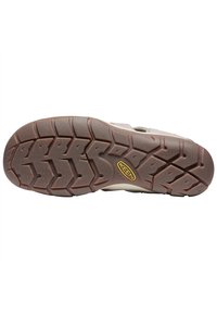 Outsole of a shoe, featuring a brown rubber tread with a zigzag pattern and a logo. The design supports traction and durability.