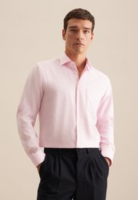 Helles rosa Hemd mit Knopfleiste und Tasche, langen Ärmeln und klassischem Kragen, kombiniert mit dunklen Hosen. Glatte Stoffoberfläche.