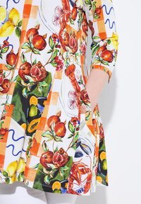 Tunique colorata caratterizzata da un motivo floreale e fruttato, principalmente in arancione e verde, con maniche 3/4 e vestibilità ampia, completa di tasche laterali.