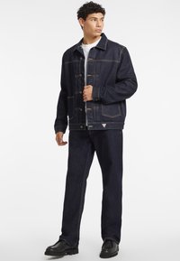 Dark denim jacket with a button-front, two chest pockets, and contrasting stitching. Paired with matching dark denim pants and black shoes.