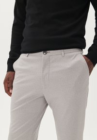 Világosszürke nadrág texturált anyagból, lapos elejű, oldalzsebekkel és elülső gombos záródással. Fekete pulóverrel viselve.