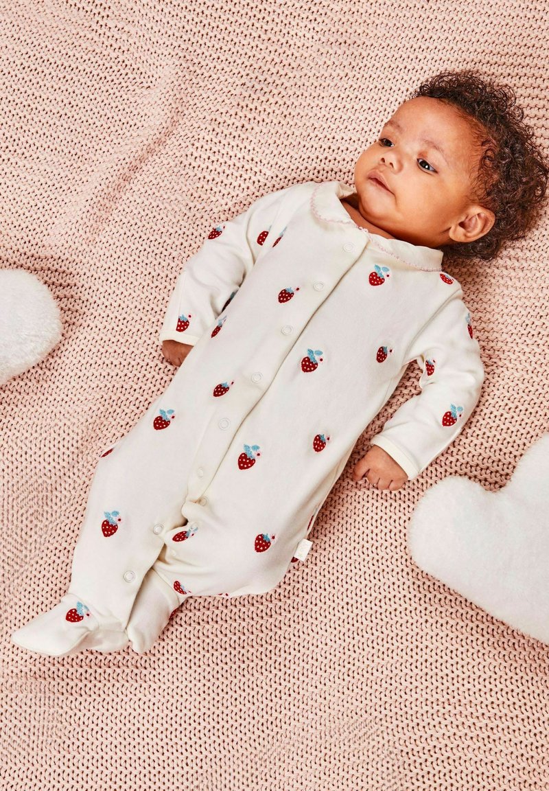 Body neonato bianco con motivo di fragole rosse, dotato di colletto arrotondato e chiusure a scatto, posato su una coperta rosa strutturata.