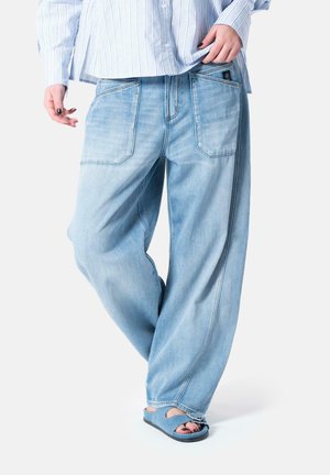 Lyseblå denimjeans med løs passform, fem lommer og sømdetaljer. Kombinert med blå sandaler, som viser en avslappet stil.