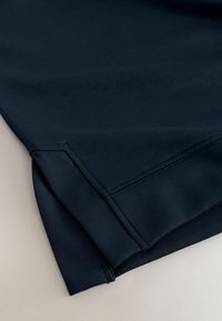 Dunkelmarineblaue Stoff mit einem kleinen seitlichen Schlitz und einem verstärkten doppelt genähten Saum auf einer glatten hellen Oberfläche.