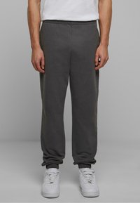 Grå sweatpants med elastisk talje og afsluttede nederste kanter, lavet af et blødt stof. Har en afslappet pasform, parret med hvide sneakers.