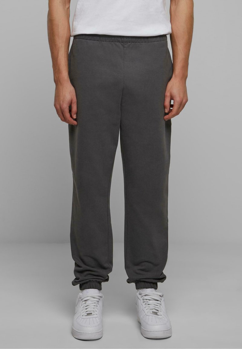 Grå sweatpants med elastisk talje og afsluttede nederste kanter, lavet af et blødt stof. Har en afslappet pasform, parret med hvide sneakers.