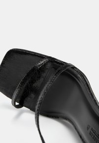 Sandale negre cu toc, cu un superior sintetic lucios, având trei curele subțiri pe picior și un design cu vârful pătrat.