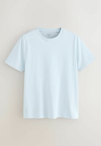 T-shirt bleu clair à manches courtes et col rond, taille moyenne, suspendu devant un fond beige neutre.