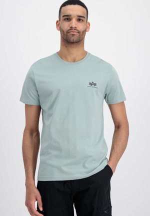 Tricou de bumbac, verde deschis, cu mânecă scurtă, având un guler rotund și un mic logo negru pe piept. Fără modele sau grafice.