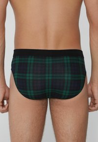 Herren-Schwimmslips in einem schwarz-grünen Karomuster. Verfügt über ein nahtloses Design mit einem schwarzen elastischen Bund. Weiches, strukturiertes Material.