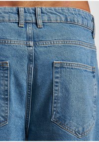 Pantalones cortos de mezclilla azul claro con una cintura de altura media, costuras visibles y dos bolsillos traseros. La tela tiene un acabado suave y texturizado.