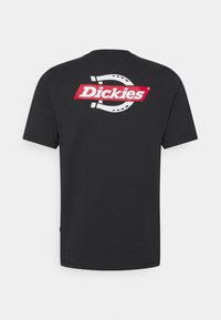 Camiseta de algodón negra con un gran herradura blanca y el logo "Dickies" en rojo en la parte posterior. Con mangas cortas y cuello redondo.