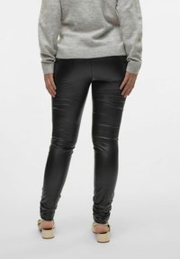 Zwarte neplederen leggings met een gladde, glanzende textuur en een aansluitend ontwerp. Ggedragen met een grijze trui en beige sandalen.