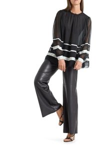 Blouse noire transparente avec des rayures blanches horizontales, manches longues et col rond. Associée à un pantalon en cuir noir ajusté et des talons à lanières.