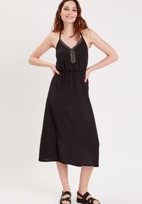 Robe maxi noire avec fines bretelles, décolleté en V et détails texturés au niveau de la poitrine. Taille élastique, tissu fluide et longueur jusqu'aux chevilles.