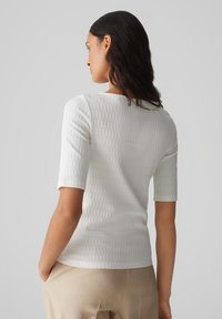 Witte geribbelde gebreide top met korte mouwen en een ronde halslijn, met subtiele verticale textuur, gecombineerd met lichtbeige broeken.