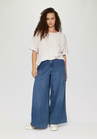 Weite blaue Jeanshose mit zwei vorderen Taschen, kombiniert mit einem locker sitzenden, creme- und braun gestreiften Kurzarmoberteil.
