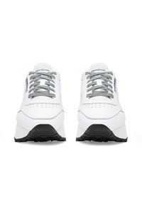 Fehér sportcipők fekete-fehér kockás fűzővel, sima bőr felsőrész, lekerekített orr és texturált fekete gumi talp. A Reebok logó jól látható.