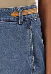 Jeansskjørt med en mid-blue vask, kontrastfarget oransje søm og en brun lærdetalj i livet. Enkelt, tettsittende design.