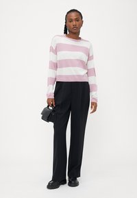 Gestreifter Pullover in Rosa und Weiß, cropped Design, kombiniert mit schwarzen weit geschnittenen Hosen und einer kleinen schwarzen Handtasche. Glatte Textur.