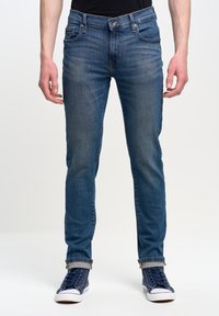 Tmavě modré džíny s úzkým střihem, se zapínáním na knoflíky, pěti kapsami a ohrnutými manžetami, doplněné námořnickými vysokými teniskami.