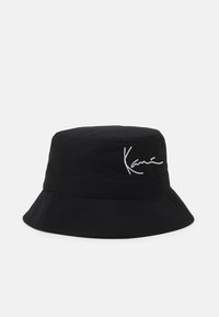 Schwarzer Bucket Hat aus Baumwolle mit einer leicht strukturierten Oberfläche. Mit einer weißen gestickten Signatur auf der Vorderseite.