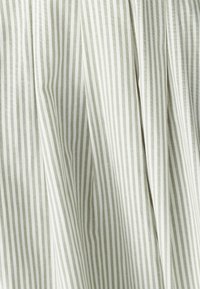 Světle zelená a bílá pruhovaná látka s vertikálními pruhy, která má hladkou texturu a jemné záhyby, vytvářející plynulý vzhled.