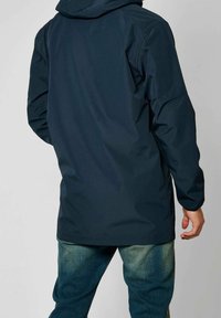 Tmavě modrá nepromokavá bunda s kapucí, s elegantním designem, dlouhými rukávy a hladkou texturou. Pohled zezadu ukazuje prodlouženou délku.