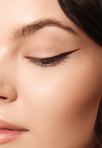 Primo piano di un occhio con una marcata eyeliner nero a forma di ala. Texture della pelle liscia, fondotinta leggero, colore delle labbra naturale e sopracciglia ben curate.