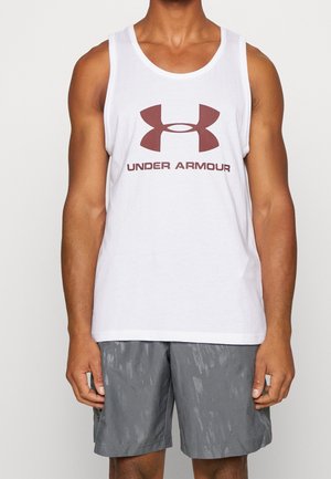 Homme portant un débardeur blanc Under Armour avec un grand logo marron et du texte, associé à un short de sport gris.