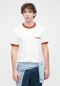 Λευκό βαμβακερό μπλουζάκι με κόκκινο ριμπ γιακά και μανίκια, με κεντημένο λογότυπο στο αριστερό στήθος. Σετ με μπλε φόρμες.