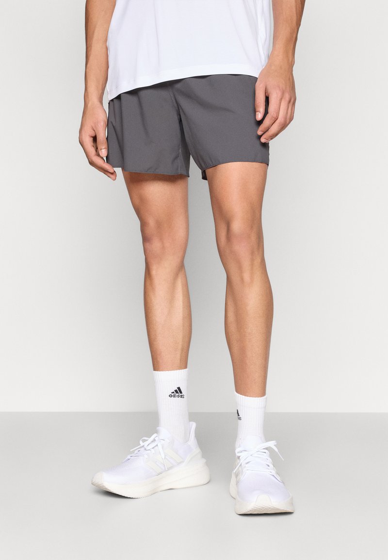 Harmaat urheilushortsit virtaviivaisella muotoilulla, yhdistettynä valkoisiin sukkiin ja valkoisiin lenkkareihin, joissa on vaaleanharmaat yksityiskohdat ja teksturoidut pohjat.