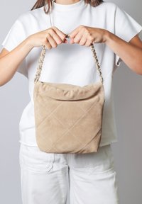 Borsa in suede beige con design trapuntato, tracolla a catena e parte superiore arricciata. Texture liscia e forma rettangolare.