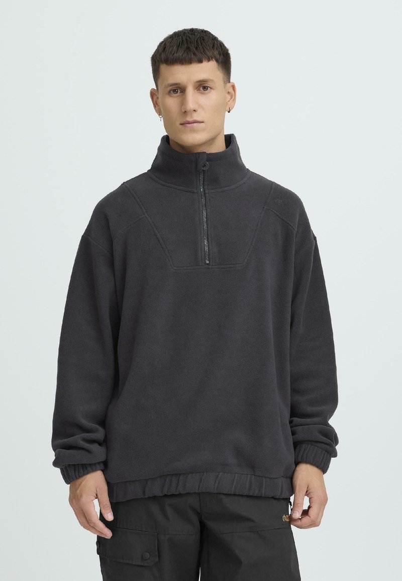 Tumehall fleece-pusa kõrge kraega, esiküljel pool lukku, soonikkoes mansettide ja äärega, tekstuurse kangaga ja avara lõikega.