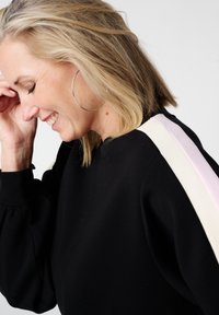 Zwarte sweatshirts met ballonmouwen, met drie horizontale strepen in crème, lichtroze en wit over de schouders.