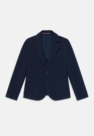 Marineblå blazer lavet af tekstureret stof, med slagkrave, to forlommer og to-knaps lukning. Indersiden er foret med en kontrastfarve.