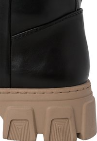 Stivale alla caviglia in pelle nera con tomaia texturizzata, suola chunky beige e dettaglio di cucitura visibile attorno alla suola e al bordo dello stivale.