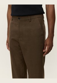 Brown checkered trousers with a smooth texture, featuring a button closure and side pockets, designed for a tailored fit.